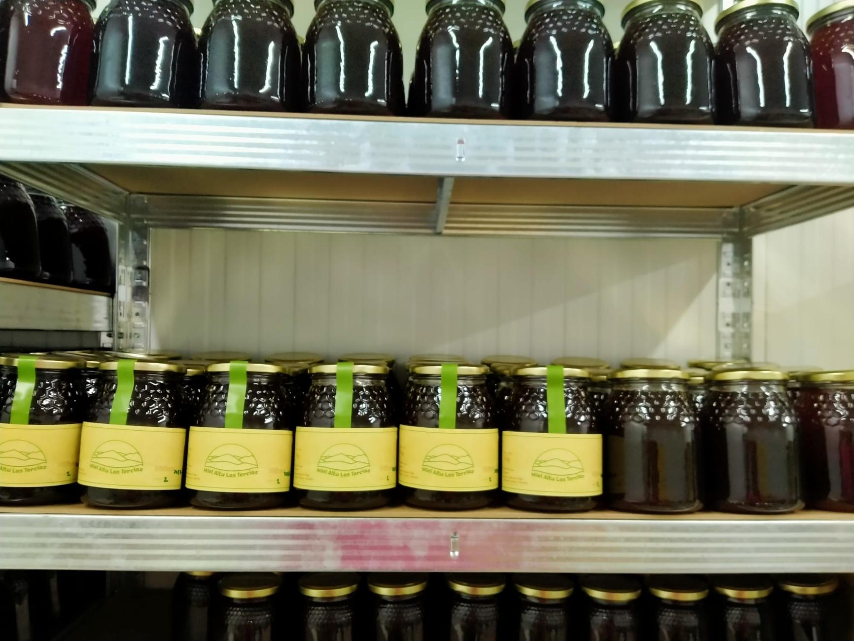 Estanterías con tarros de miel oscura. Varios llevan la etiqueta amarilla y la cinta verde.